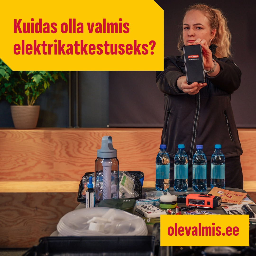 Esiplaanil laud, kus varud elektrikatkestuseks. Laua taga seisab blond naine, hoides mõlema käega akupanka, millel kiri Päästeamet. Pildi vasakul ülaservas on punasega kollasel taustal tekst: kuidas olla valmis elektrikatkestuseks? Pildi paremal allservas on punasega kollasel taustal viide: olevalmis.ee