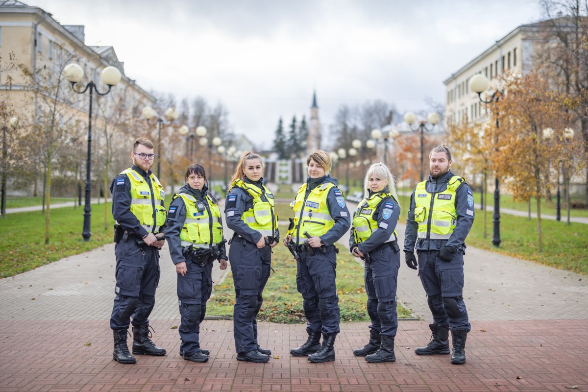 Kuus kollastes vestides abipolitseinikku pargiallee taustal kõrvuti poseerimas. Mõlemal pool äärtes on mehed, keskel neli noort naist.  pooo